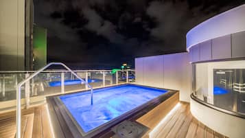 Zona de piscina exterior climatizada con barandilla de vidrio y terraza de madera.