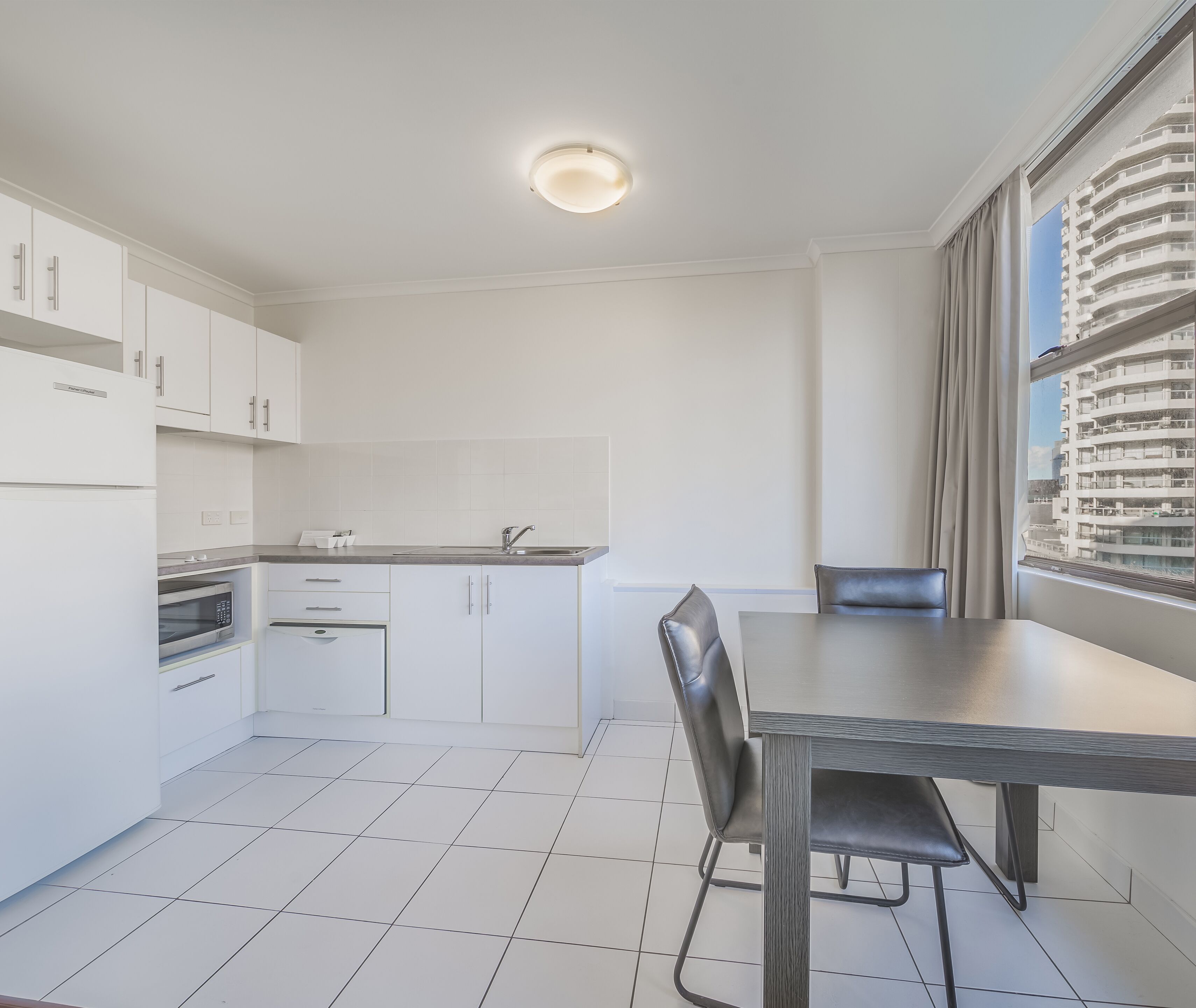 A modern kitchen with white cabinets, a built-in oven, and a dining area with a table and chairs.