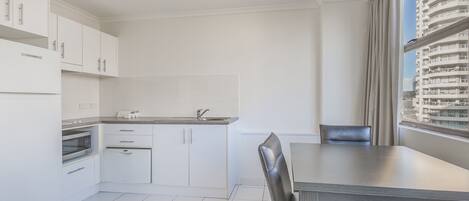 A modern kitchen with white cabinets, a built-in oven, and a dining area with a table and chairs.