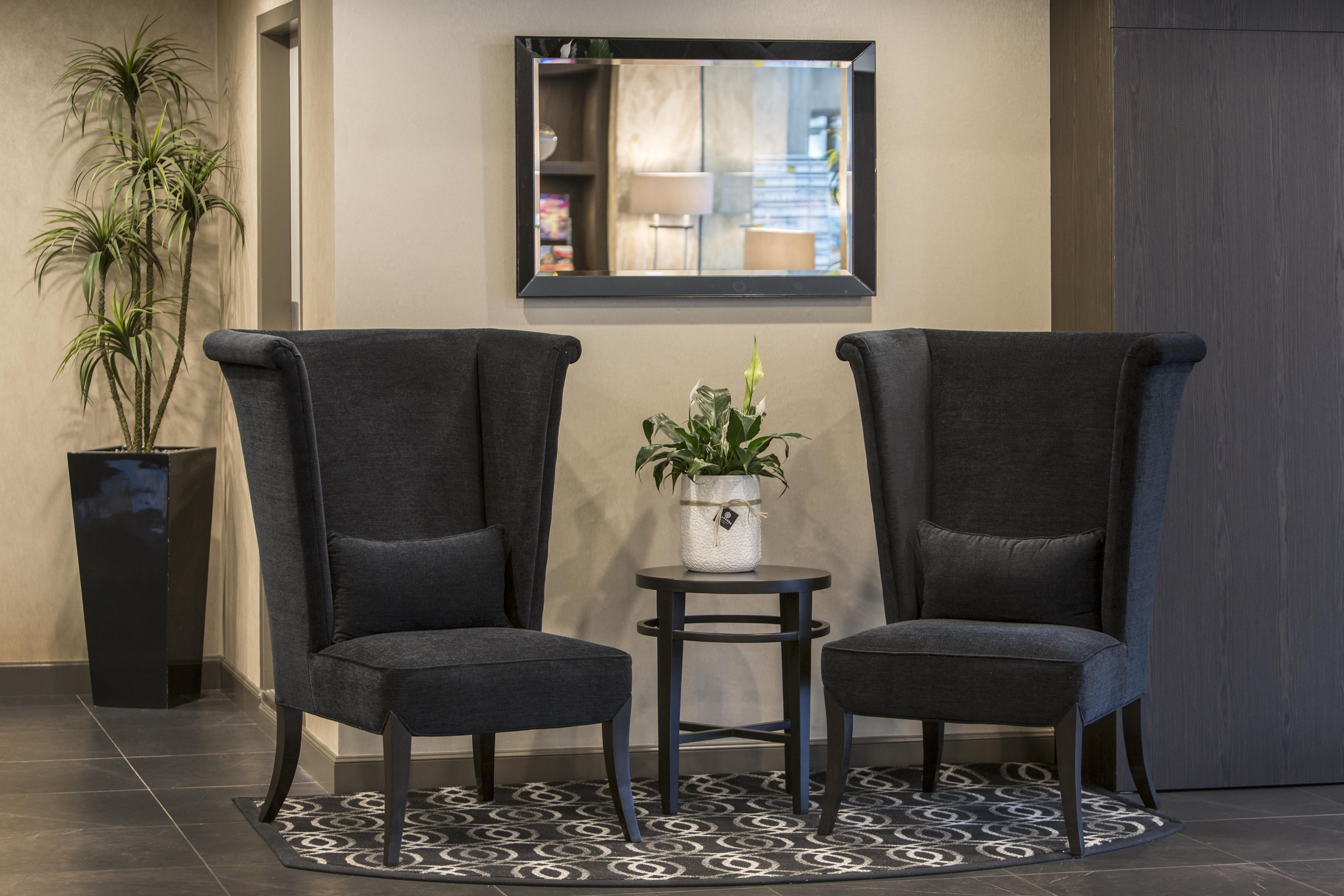 A lobby area with two armchairs, a small table, a potted plant, and a mirror on the wall.