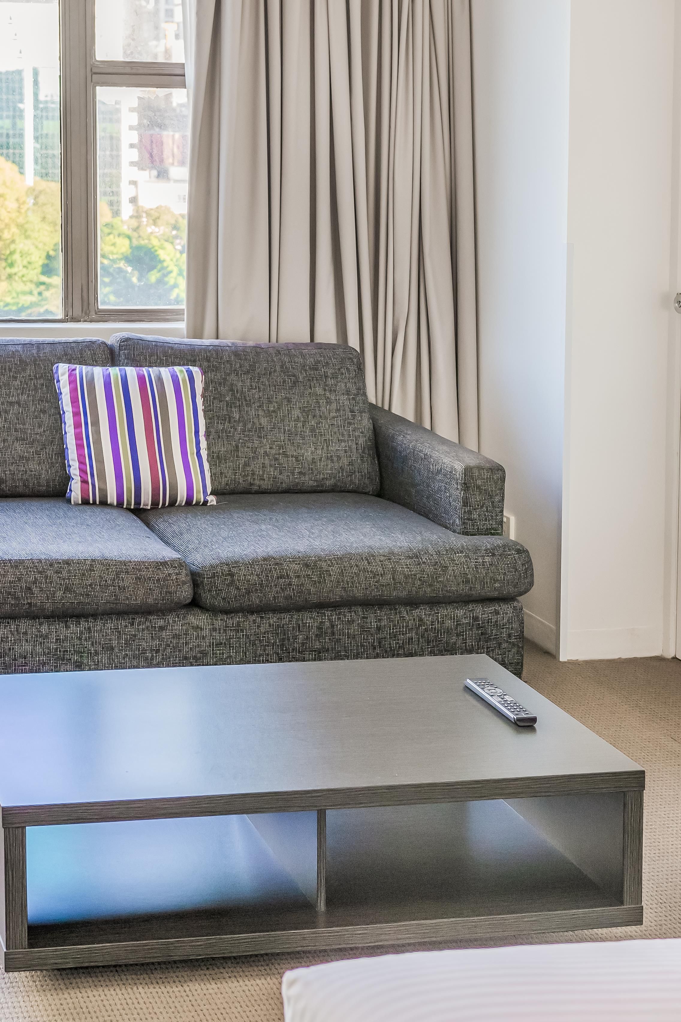 A modern living room with a grey patterned sofa, a striped pillow, and a remote control on a dark coffee table.