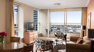 A hotel room with a balcony, a dining area, a sofa, and a television.