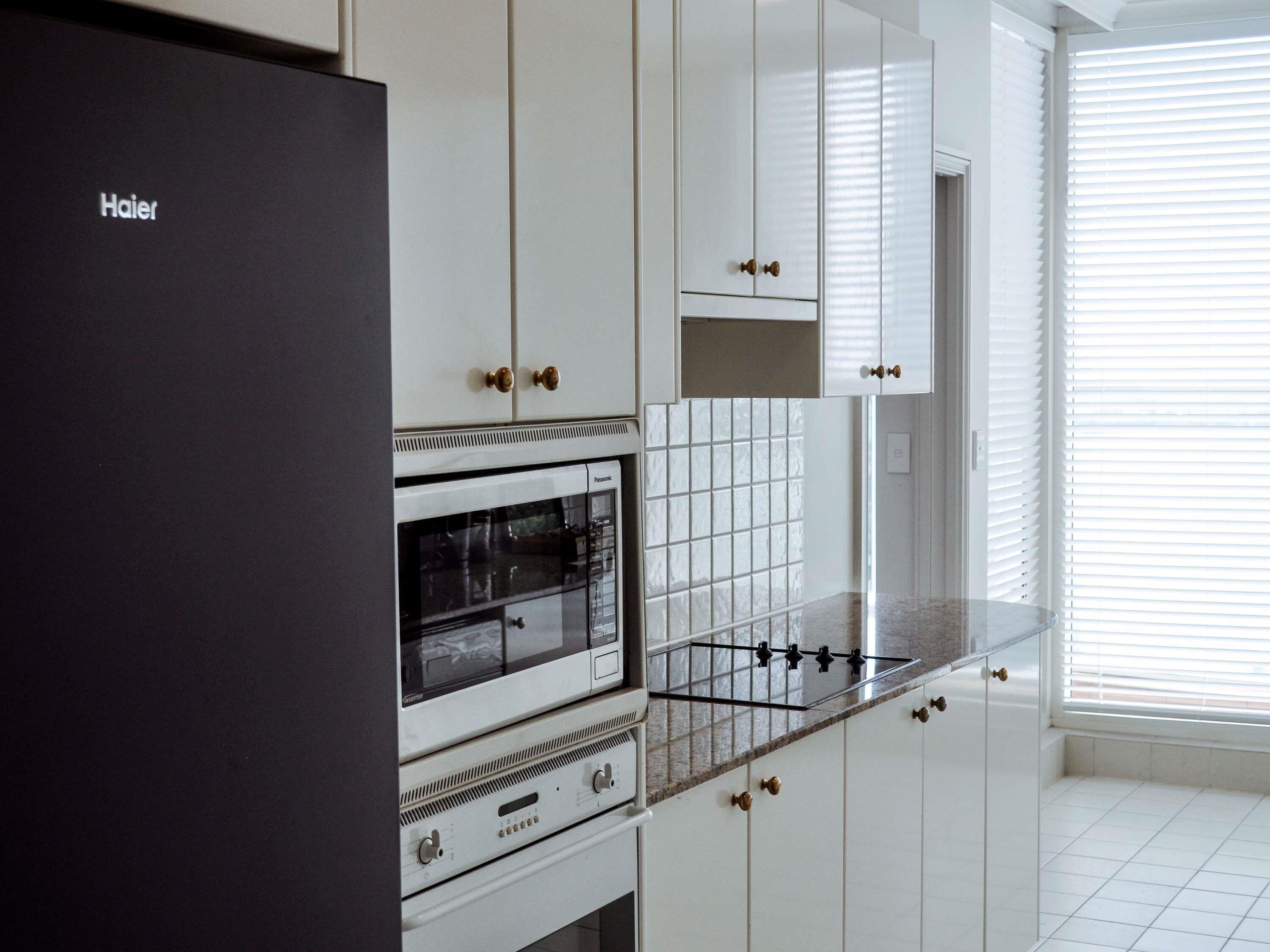 A kitchen with white cabinets, a black refrigerator, a stove, and a window with blinds.