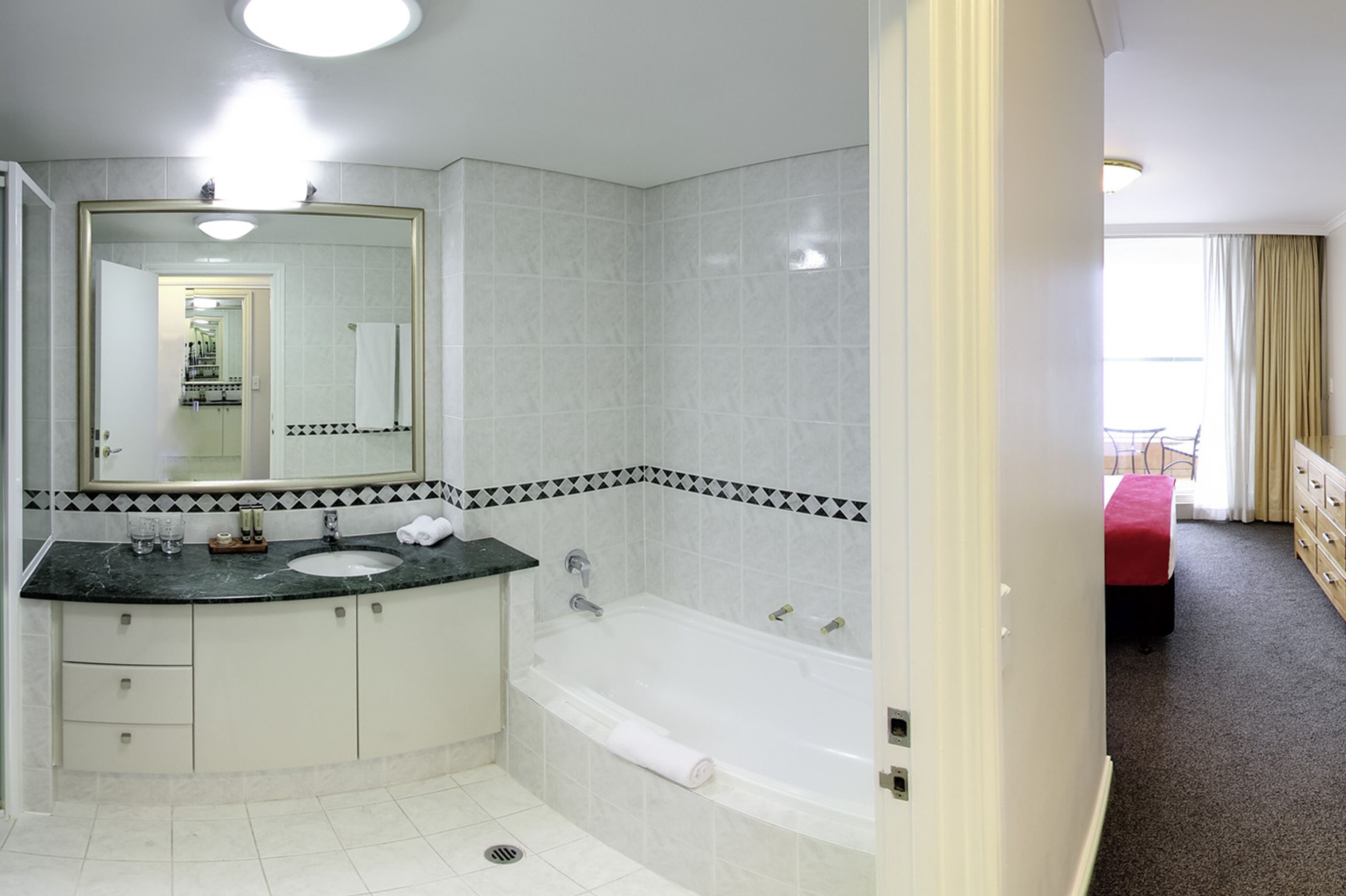 A modern bathroom with a large mirror, a sink, a bathtub, and a toilet.