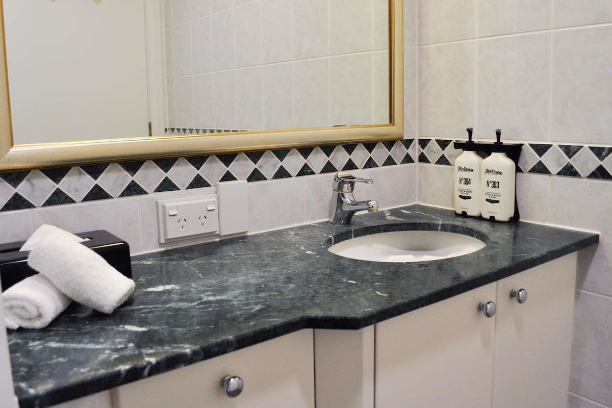 Une salle de bain avec un comptoir en marbre, un lavabo, un miroir et deux flacons de lotion.