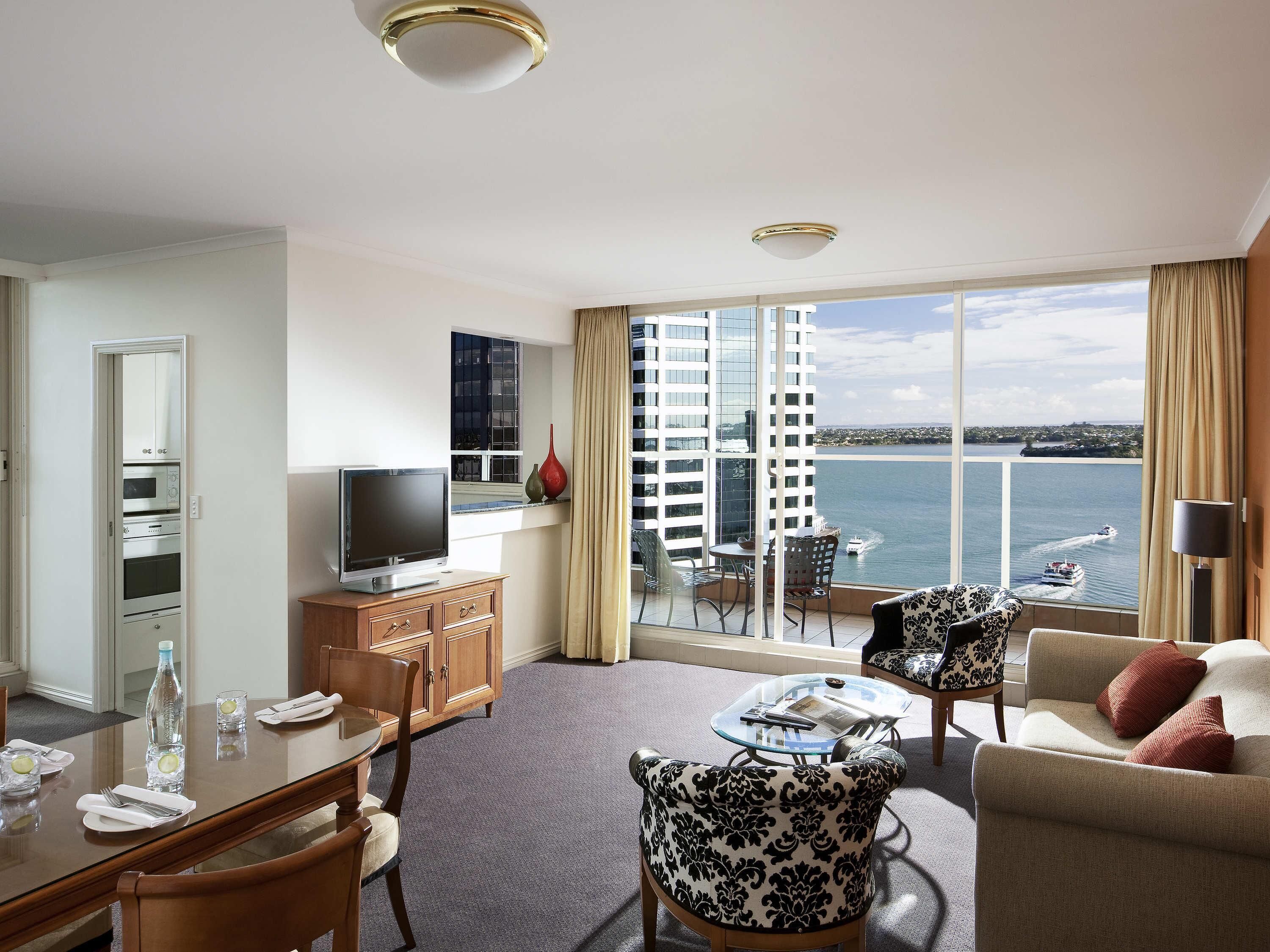 A hotel room with a balcony, a dining area, a TV, and a view of the water.