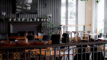 A cafe interior with wooden tables, black chairs, a TV mounted on the wall, and a 'UP CAFE' sign.