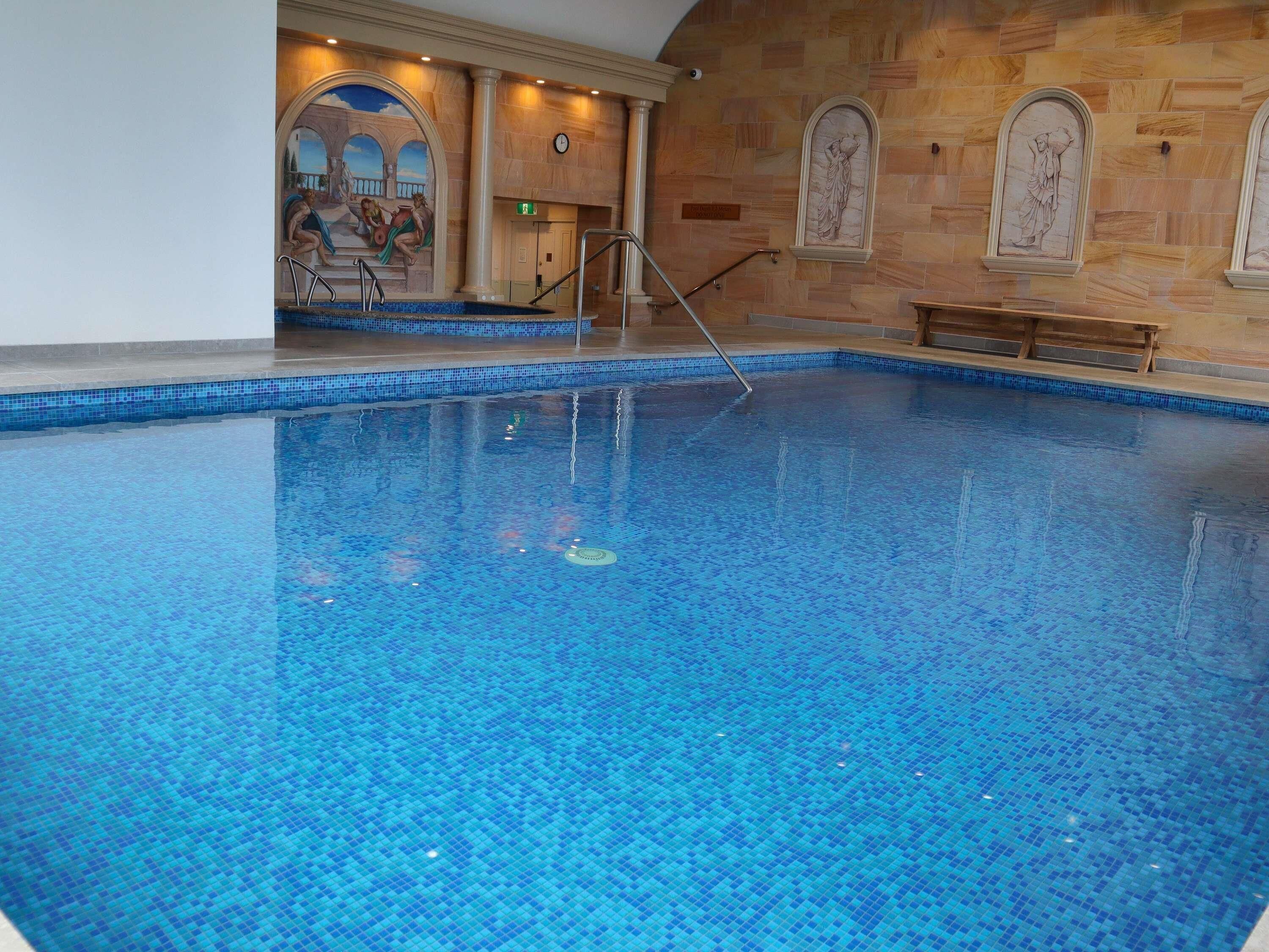Une grande piscine intérieure, ornée de mosaïques, d’une fresque murale et de sculptures classiques sur les murs.