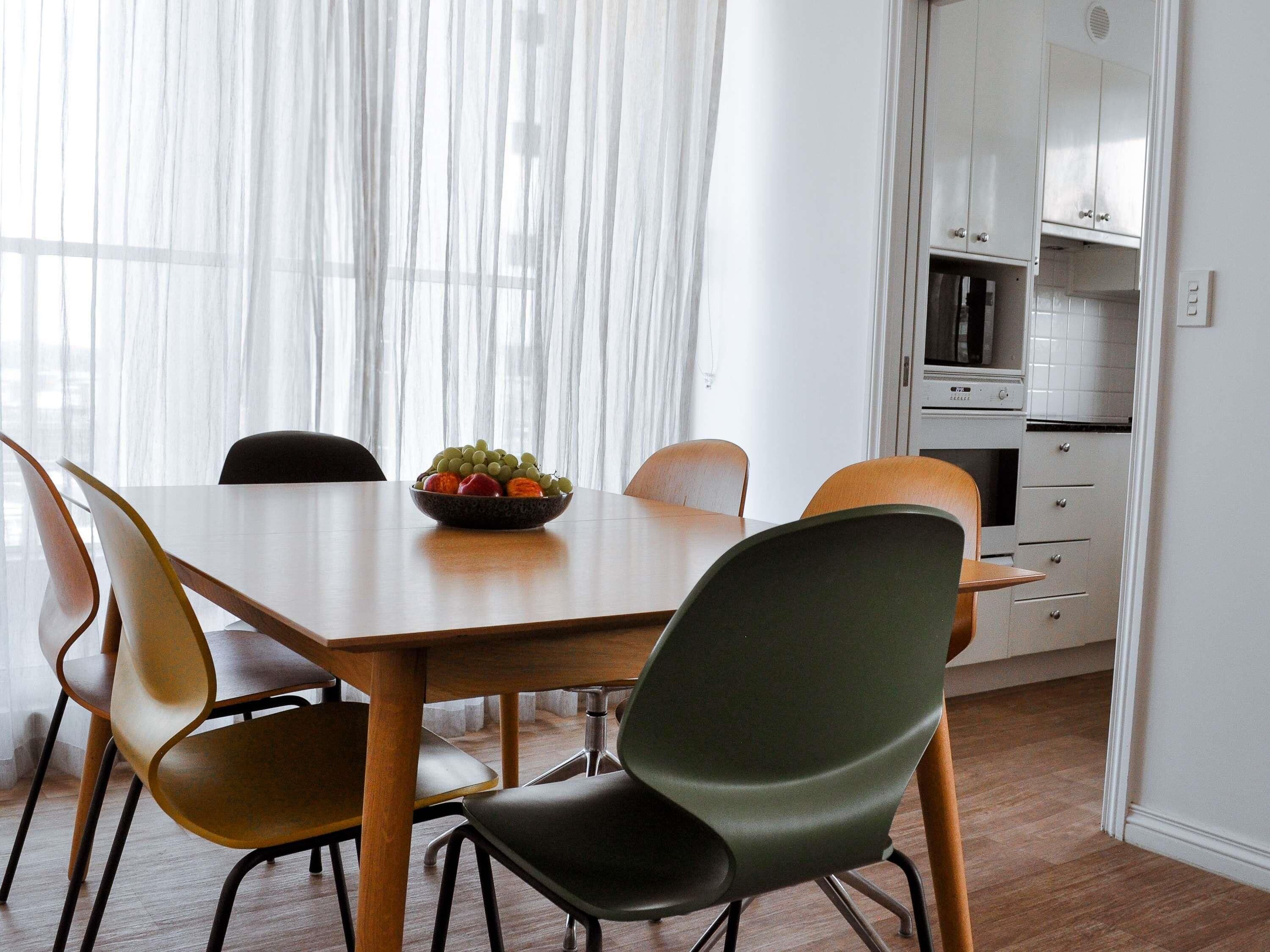 A dining area with a wooden table, four chairs, and a bowl of fruit.