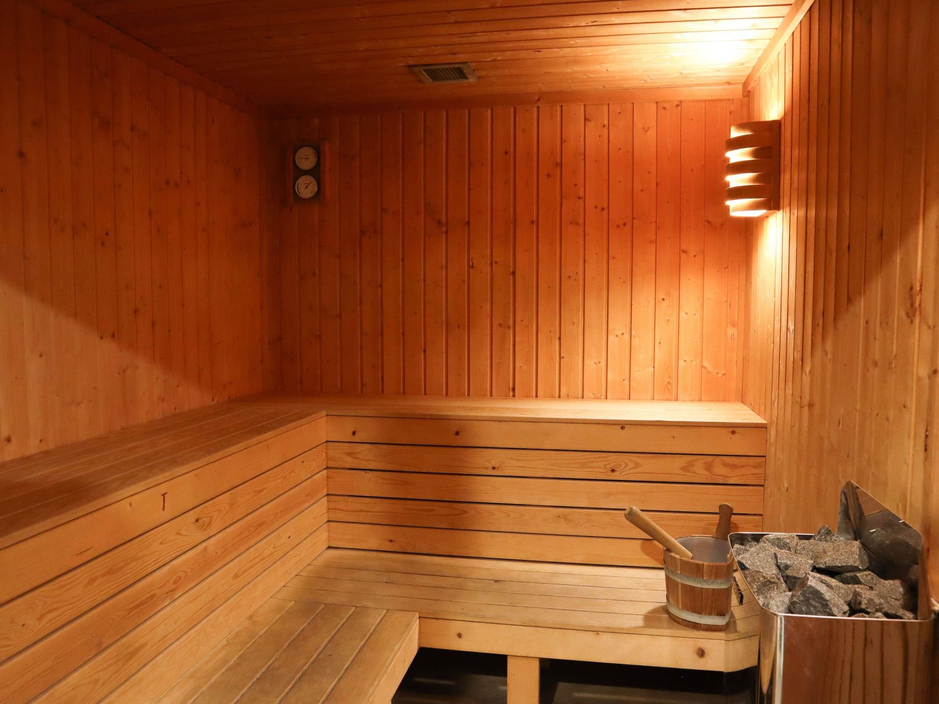 A wooden sauna with benches, a clock, and a wood-burning stove.