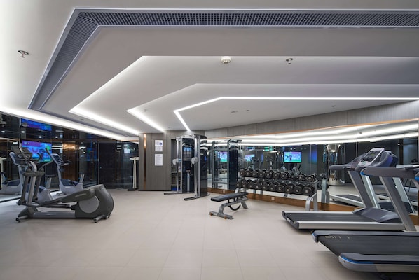 Une salle de sport moderne équipée de tapis de course, de vélos elliptiques et de poids libres.