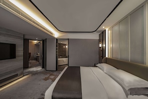 Une chambre d’hôtel moderne dotée d’un grand lit, d’un téléviseur à écran plat et d’une salle de bain visible à travers une porte ouverte.