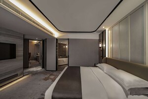 A modern hotel room with a large bed, a flat-screen TV, and a bathroom visible through an open door.