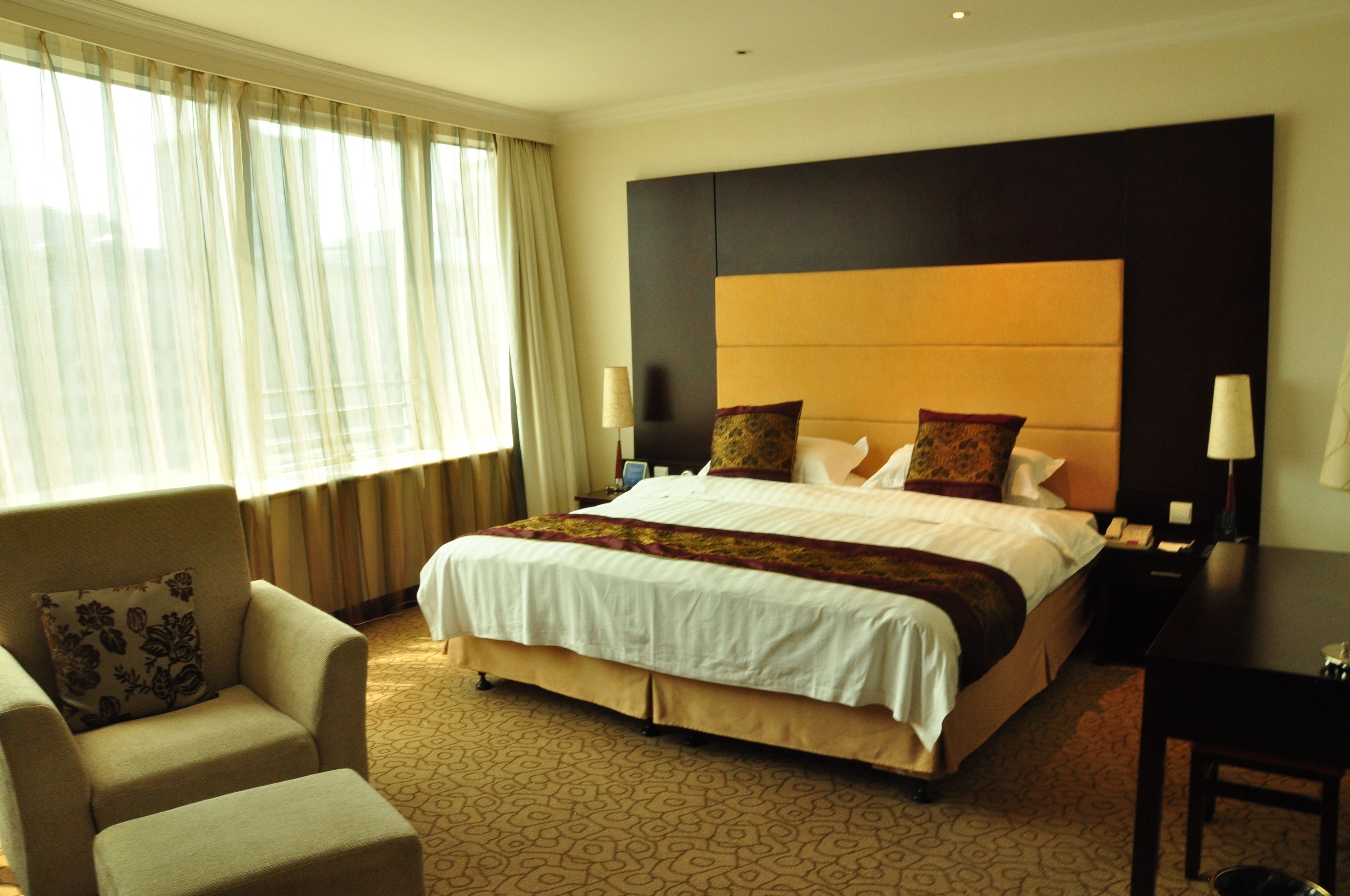 A hotel room with a large bed, a sofa, a desk, and a window with curtains.