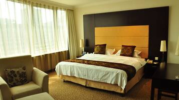 A hotel room with a large bed, a sofa, a desk, and a window with curtains.