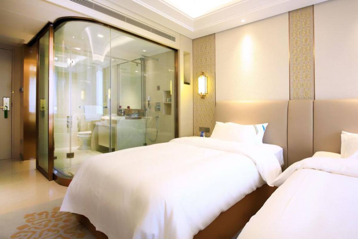 Une chambre d’hôtel avec deux lits, une douche séparée par des parois en verre et un luminaire fixé au mur.