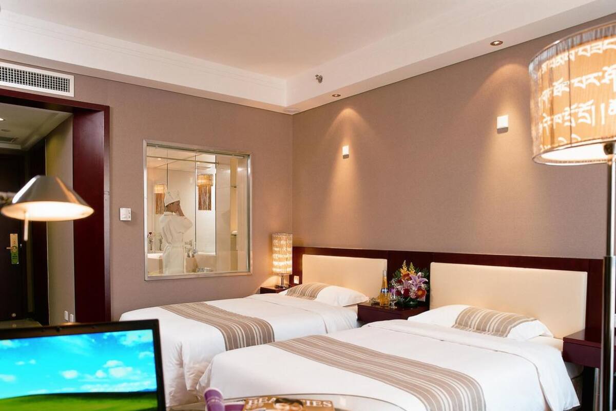 Une chambre d’hôtel avec deux lits, un bureau avec un ordinateur portable, une tasse à café et un magazine.