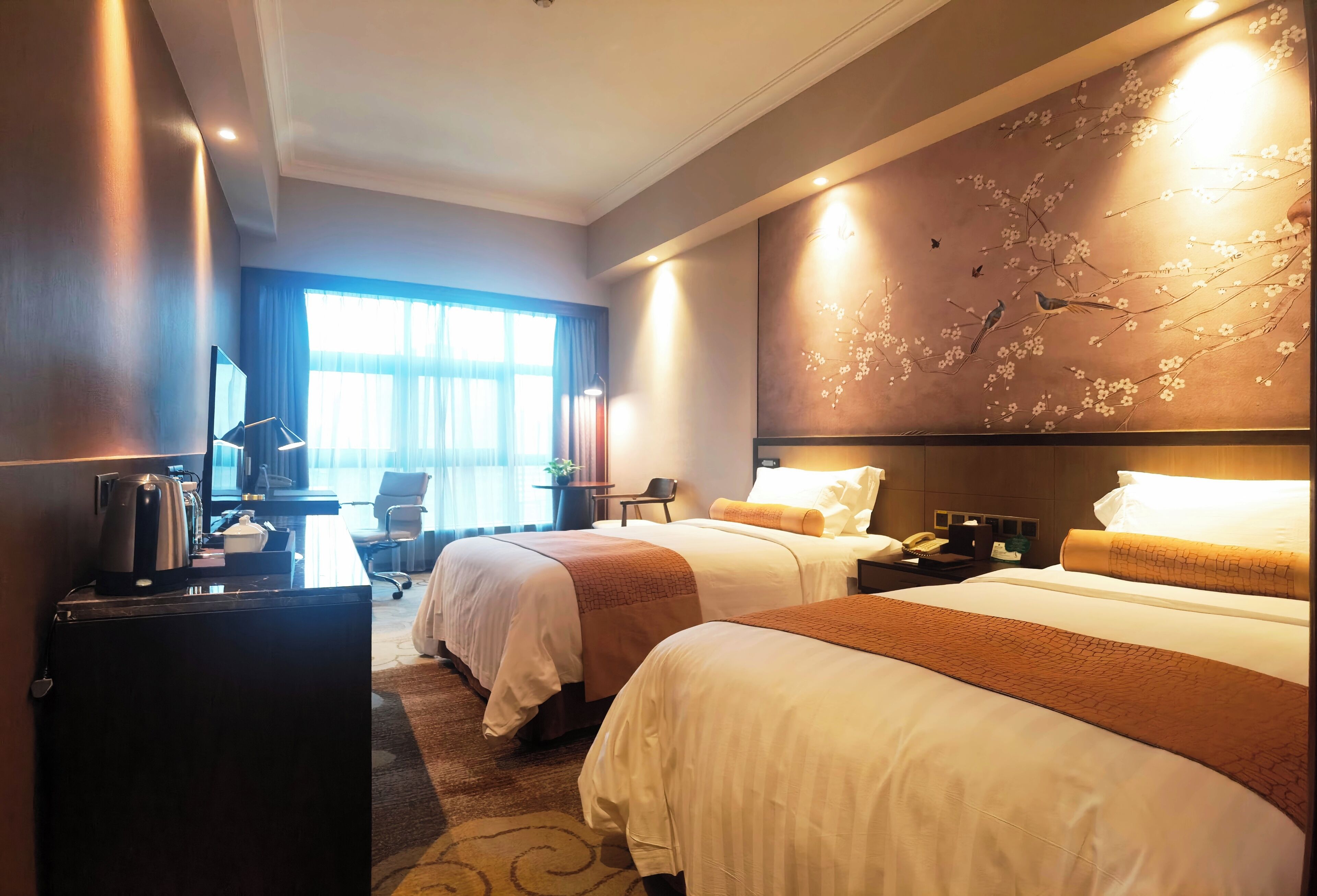 A hotel room with two beds, a desk with a computer, a coffee maker, and a TV.