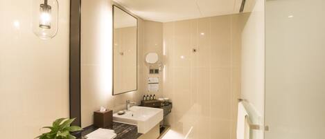 A modern bathroom with a large mirror, a sink, a shower, and a potted plant.