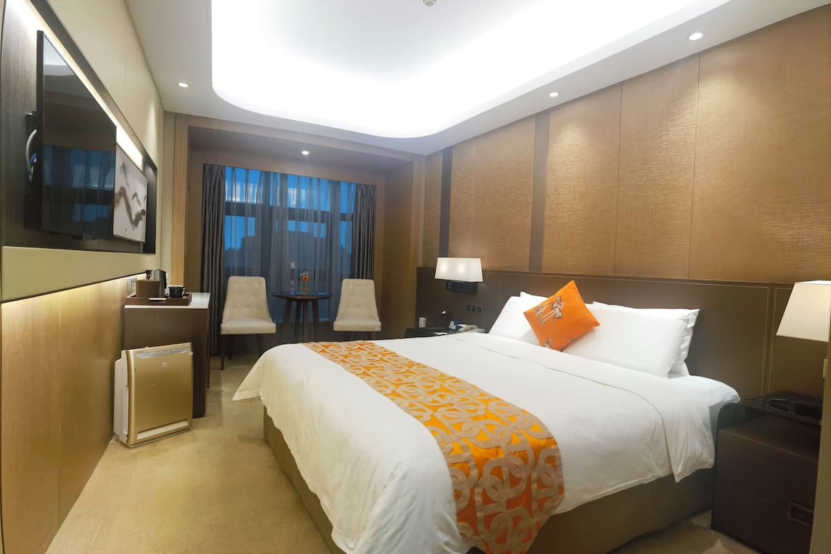 Habitación de hotel con una cama grande, un escritorio, una silla, un televisor y una ventana con cortinas.