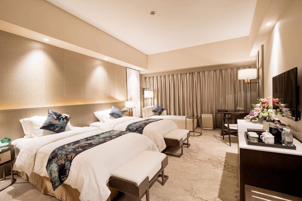 Habitación de hotel con dos camas, un escritorio, una silla, un televisor y un baño.