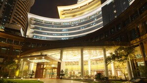 A modern hotel with a curved facade, large glass windows, and a well-lit entrance area with a fountain and landscaped garden. - Jin Jiang Pine City Hotel (Shanghai)