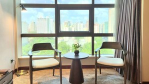 A room with two chairs and a table, large windows with a city view, and a curtain on the right. - Jin Jiang Pine City Hotel (Shanghai)