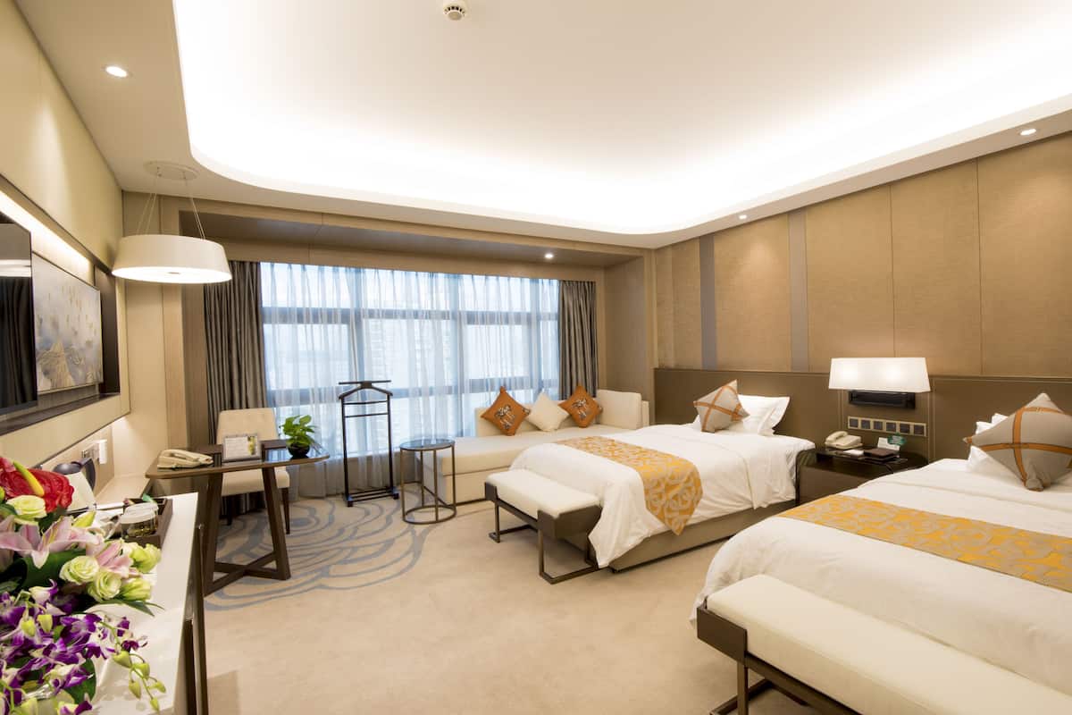 Habitación de hotel con dos camas, un escritorio, una silla, una mesita y un ventanal grande con cortinas.