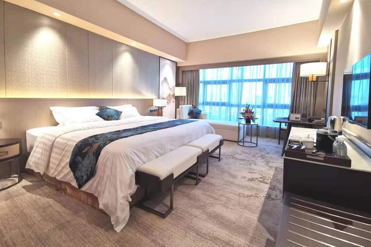 Una habitación de hotel moderna con una cama grande, mesitas de noche, un escritorio y un ventanal amplio.