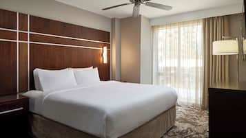 A hotel room with a large bed, a ceiling fan, a nightstand, a lamp, and a window with curtains.
