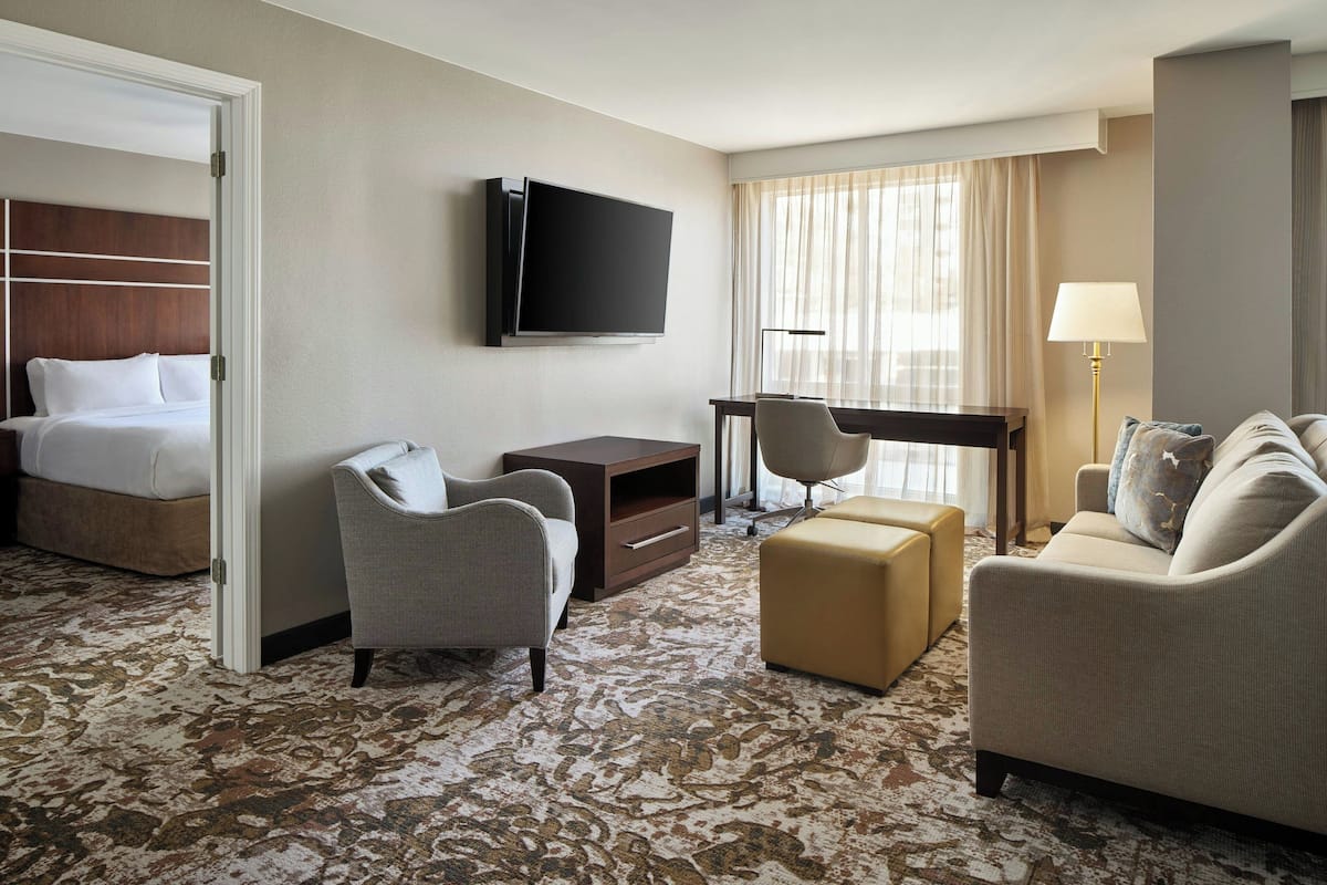 Ein Hotelzimmer mit Bett, Fernseher, Schreibtisch, Stuhl, Sofa und Lampe.