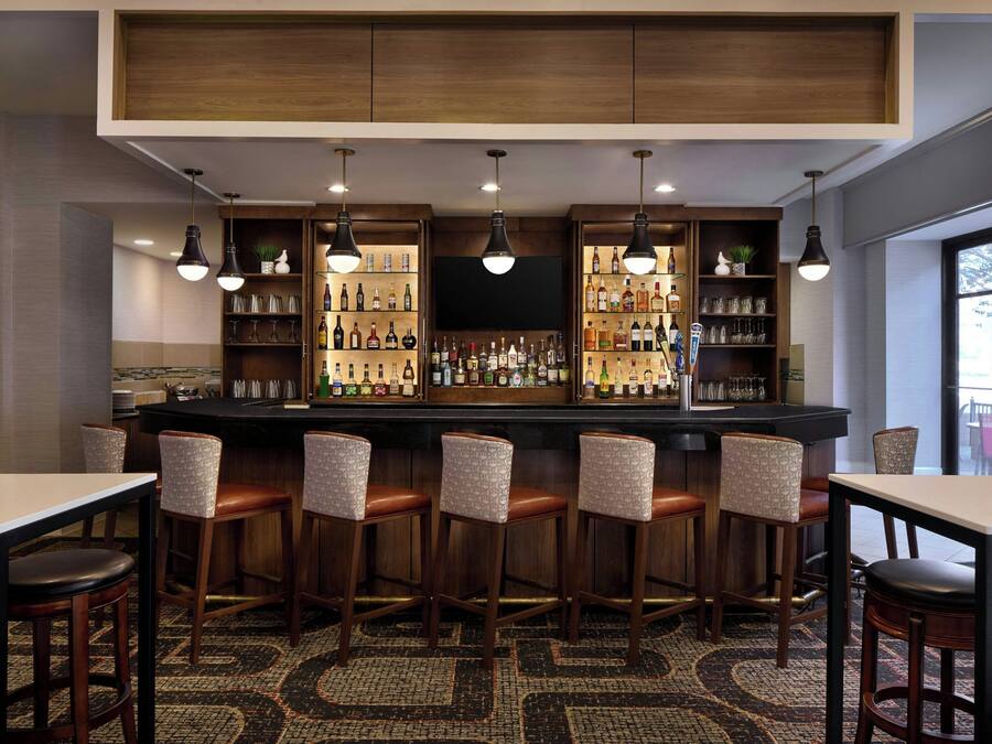 A bar area with a long counter, multiple stools, and shelves stocked with bottles.