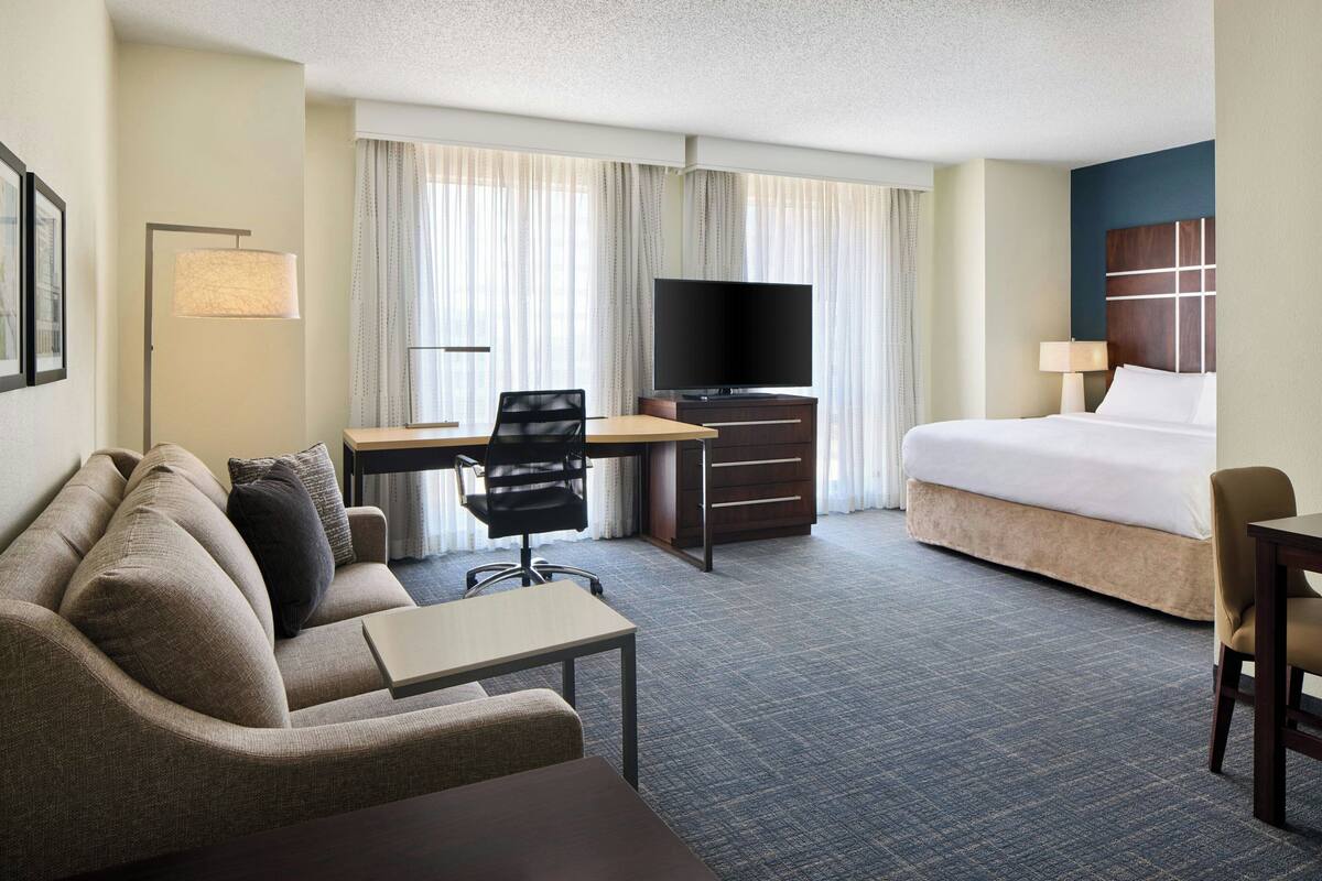 Ein Hotelzimmer mit einem Bett, einem Schreibtisch mit Stuhl, einem Fernseher und einem Sofa.