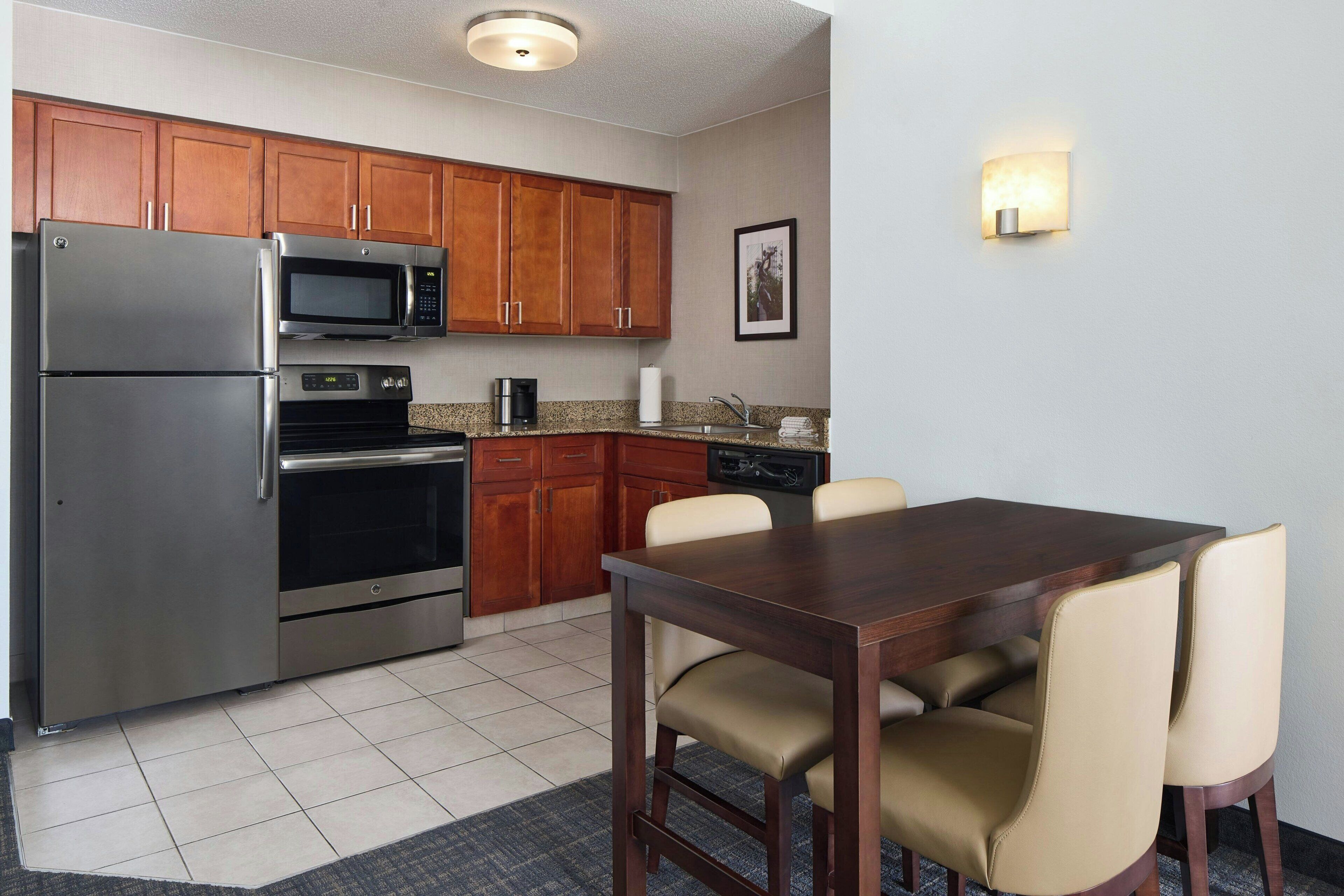 A kitchen with wooden cabinets, stainless steel appliances, a dining table with chairs, and a wall-mounted light fixture.