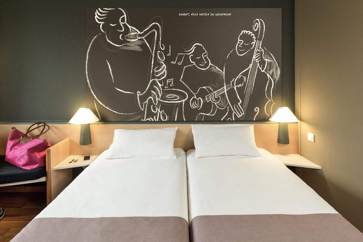 A hotel room with two beds, a wall art of musicians, bedside lamps, and a pink bag on the left nightstand.