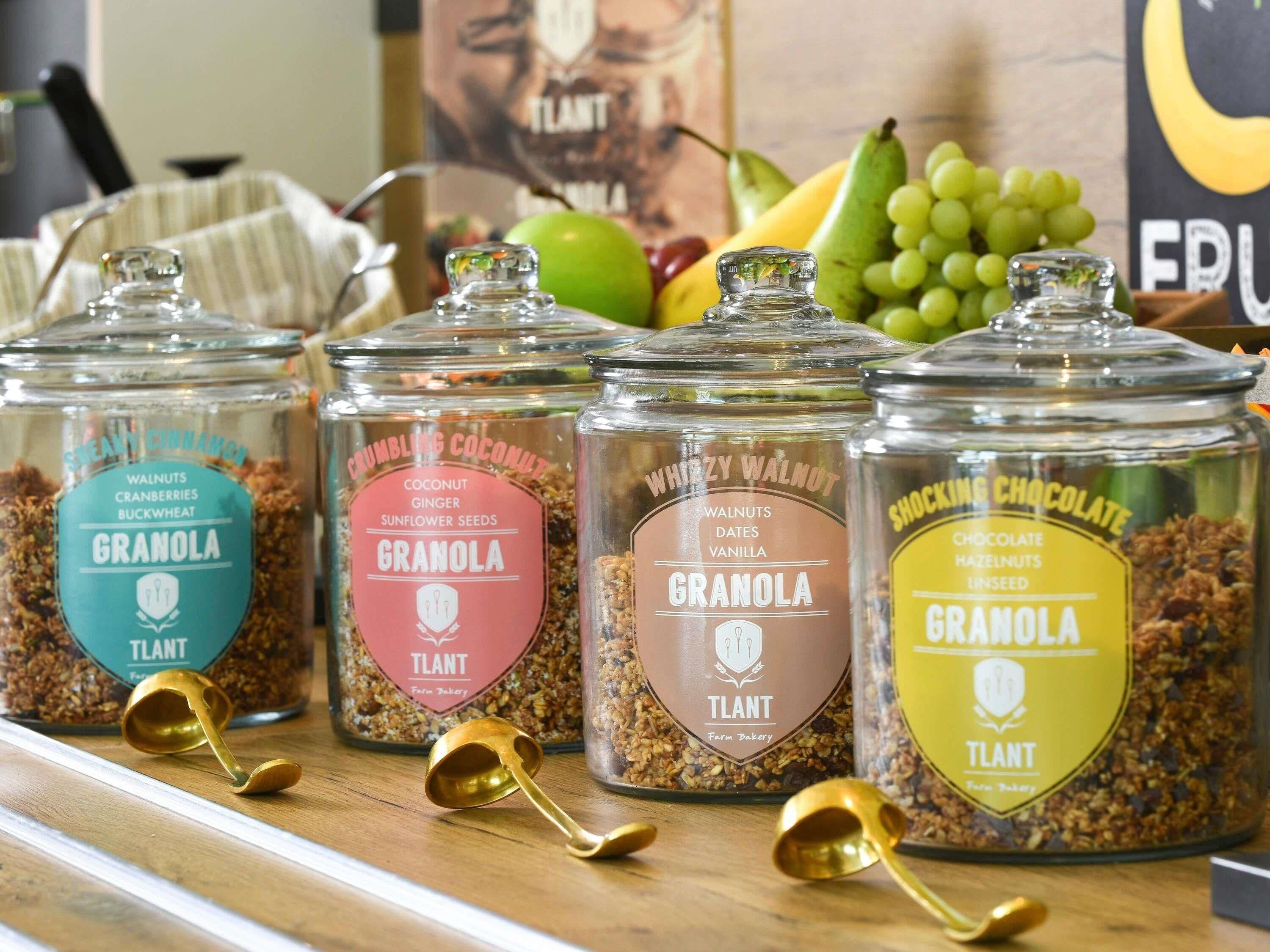 Cuatro frascos de granola con distintos sabores, cada uno etiquetado, sobre una superficie de madera.