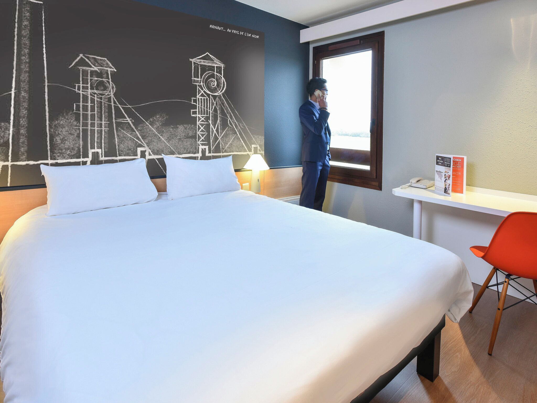 Habitación de hotel con una cama grande, un escritorio, una silla y una ventana con vistas a un edificio.