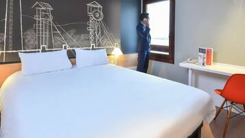 Habitación de hotel con una cama grande, un escritorio, una silla y una ventana con vistas a un edificio.