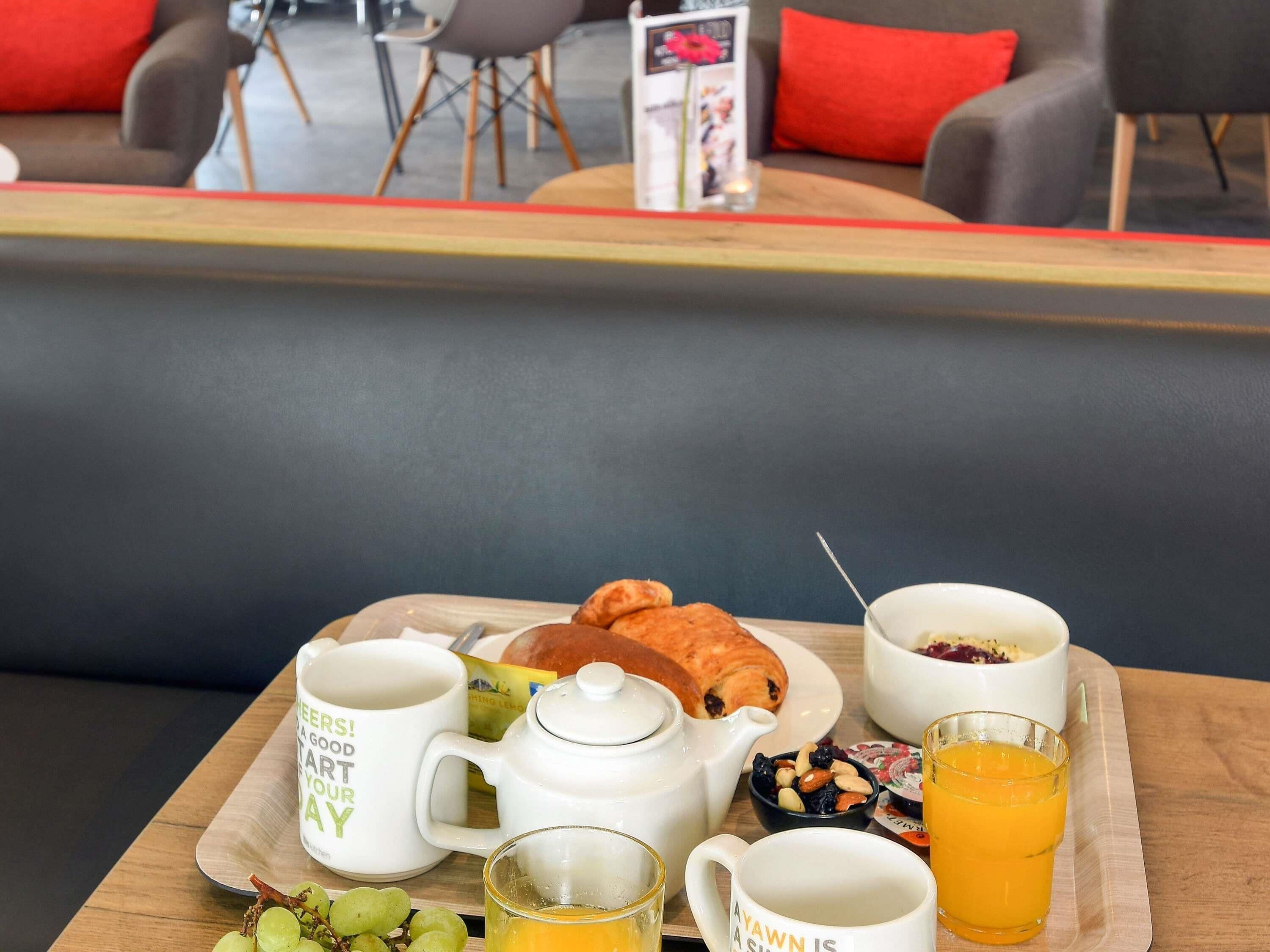 Ein Frühstücksbrett mit einem Croissant, einer Teekanne, einer Tasse, einem Glas Orangensaft und einer Schüssel Obst.