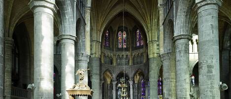 Interior de una catedral con altos techos abovedados, hileras de bancos de madera y vidrieras.