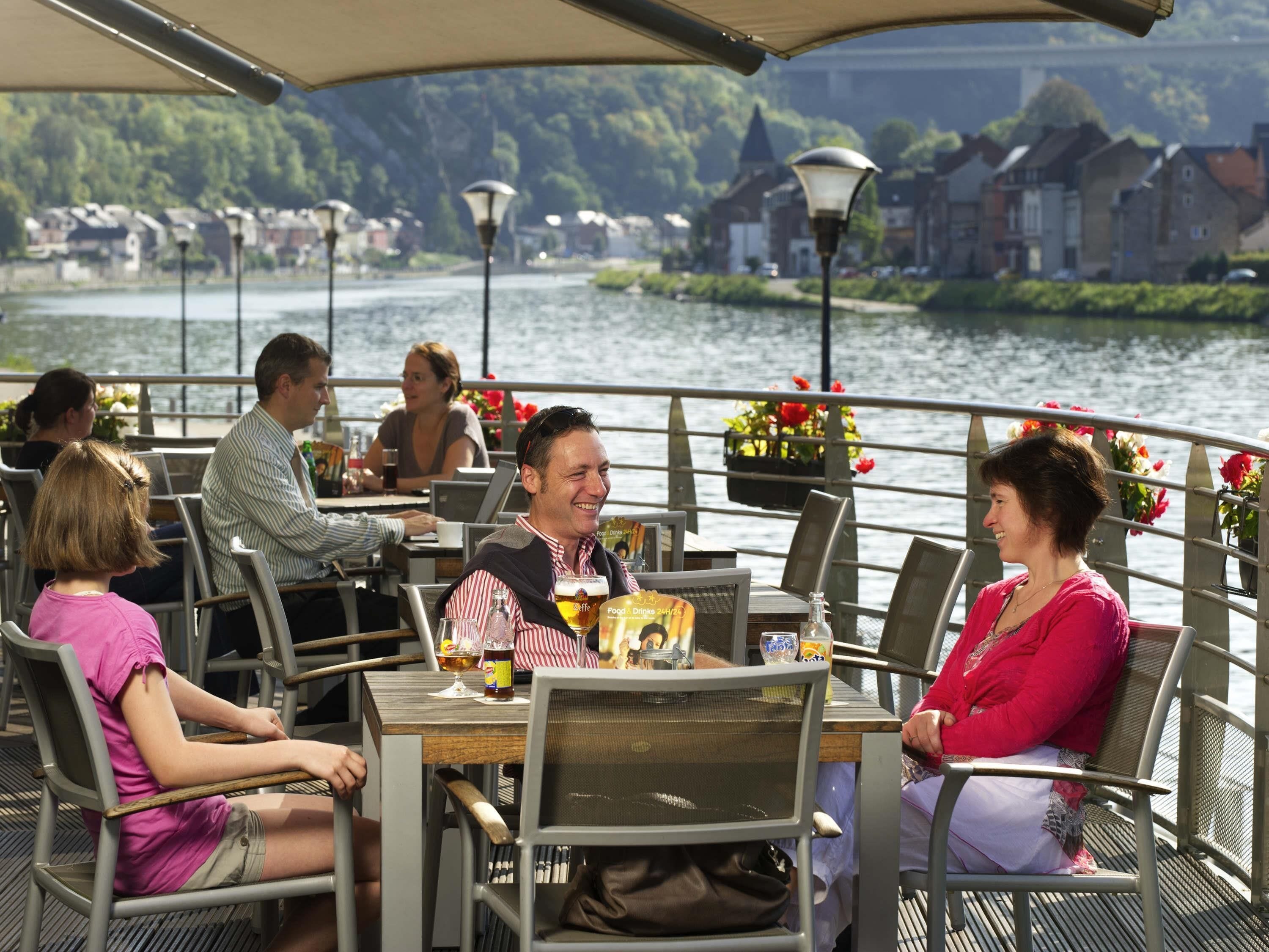 Ein Essbereich mit Tischen und Stühlen, Blick auf einen Fluss und Gebäude im Hintergrund.