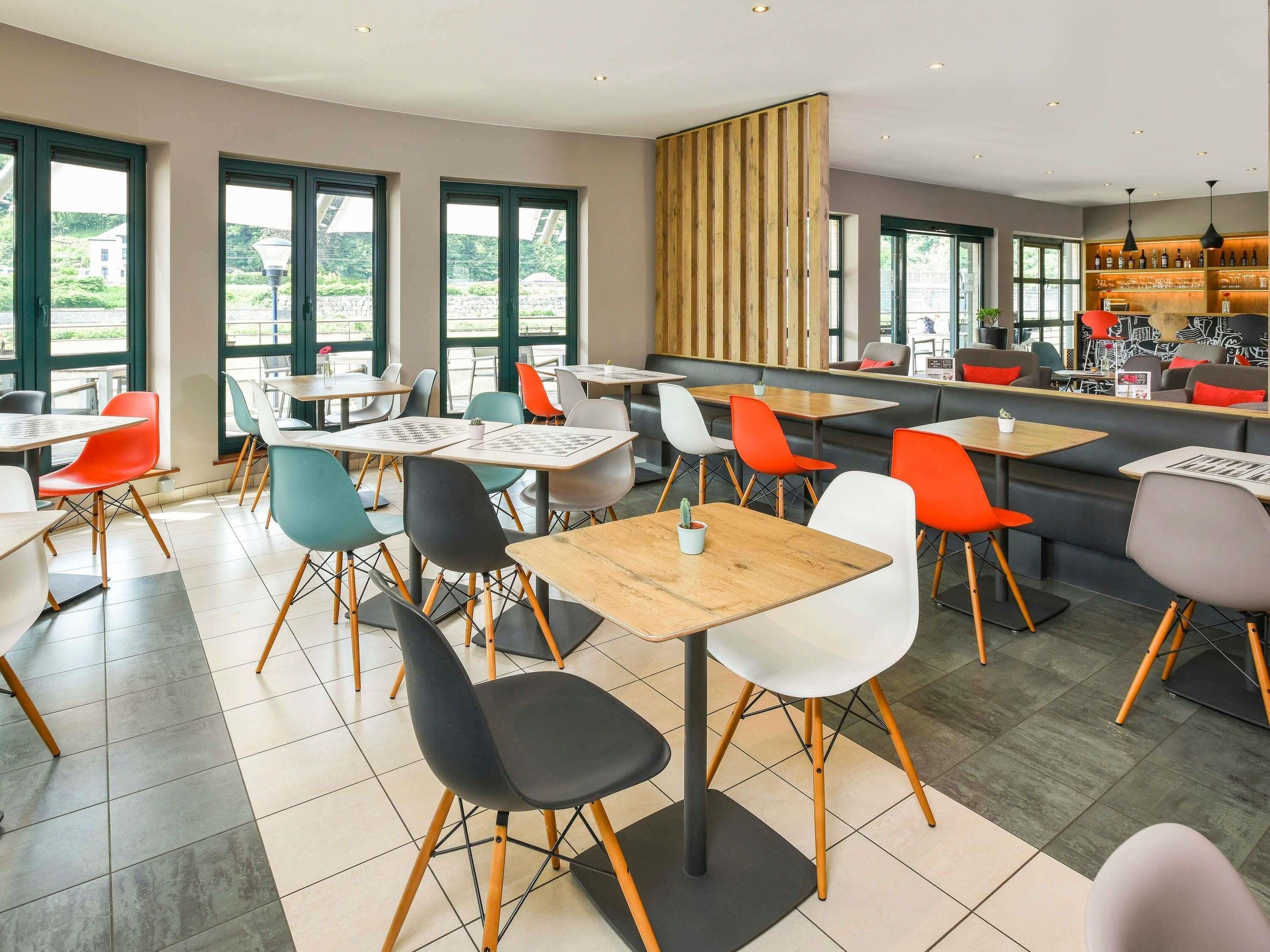 Un café moderne doté de plusieurs espaces de détente, notamment des tables et des chaises, ainsi qu’un bar avec un comptoir et des étagères.