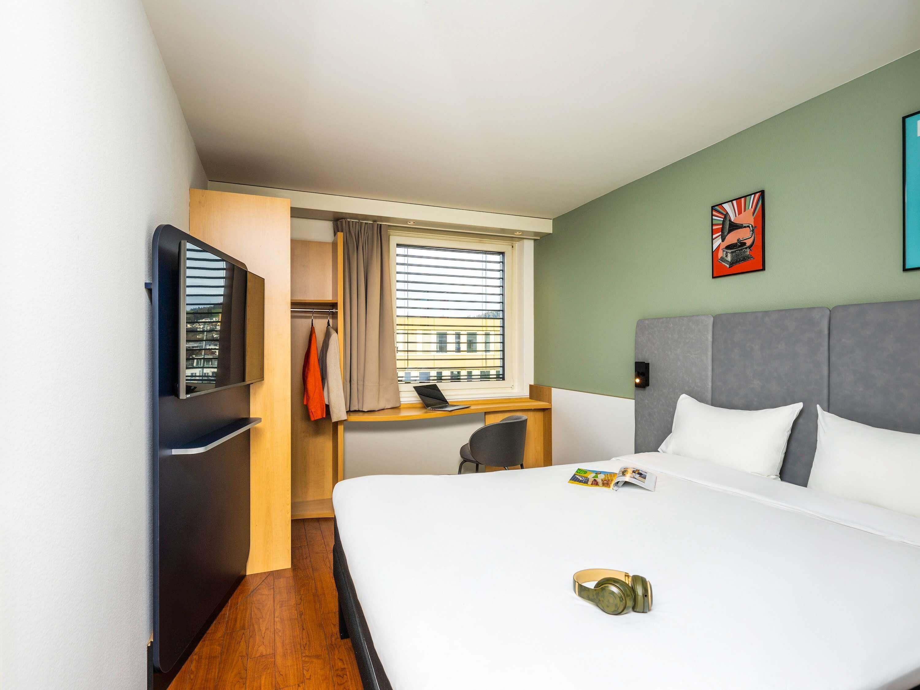 Ein Hotelzimmer mit Bett, Schreibtisch, Fernseher und einem Fenster mit Vorhängen.