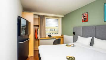 Ein Hotelzimmer mit Bett, Schreibtisch, Fernseher und einem Fenster mit Vorhängen.