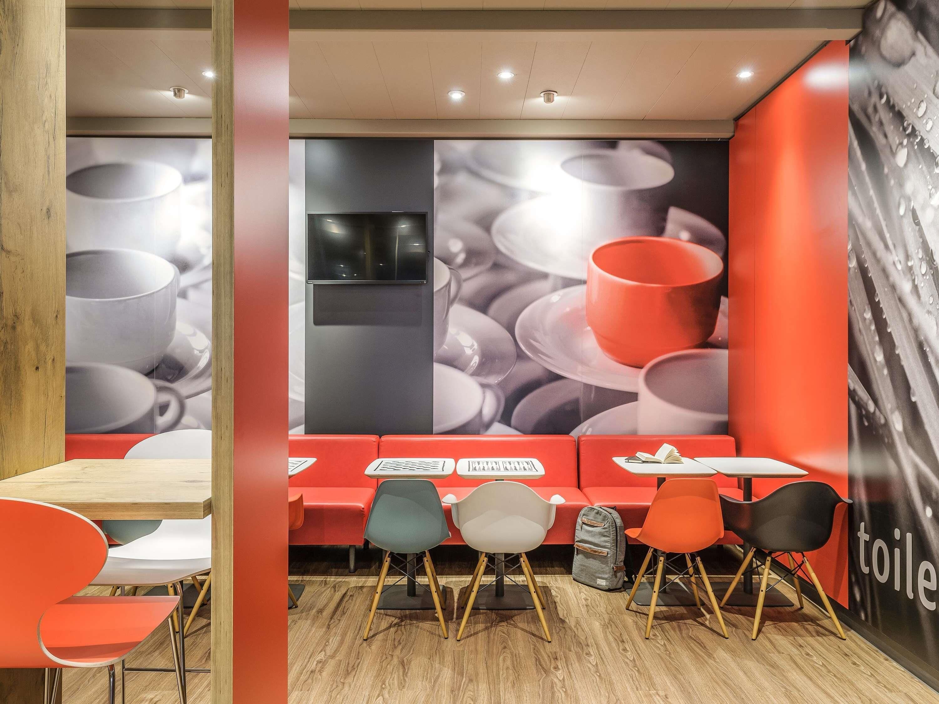 A modern cafe with a wooden floor, red seating, and a large wall mural of cups.