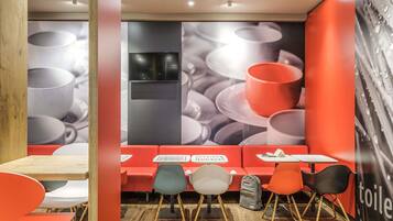 A modern cafe with a wooden floor, red seating, and a large wall mural of cups.
