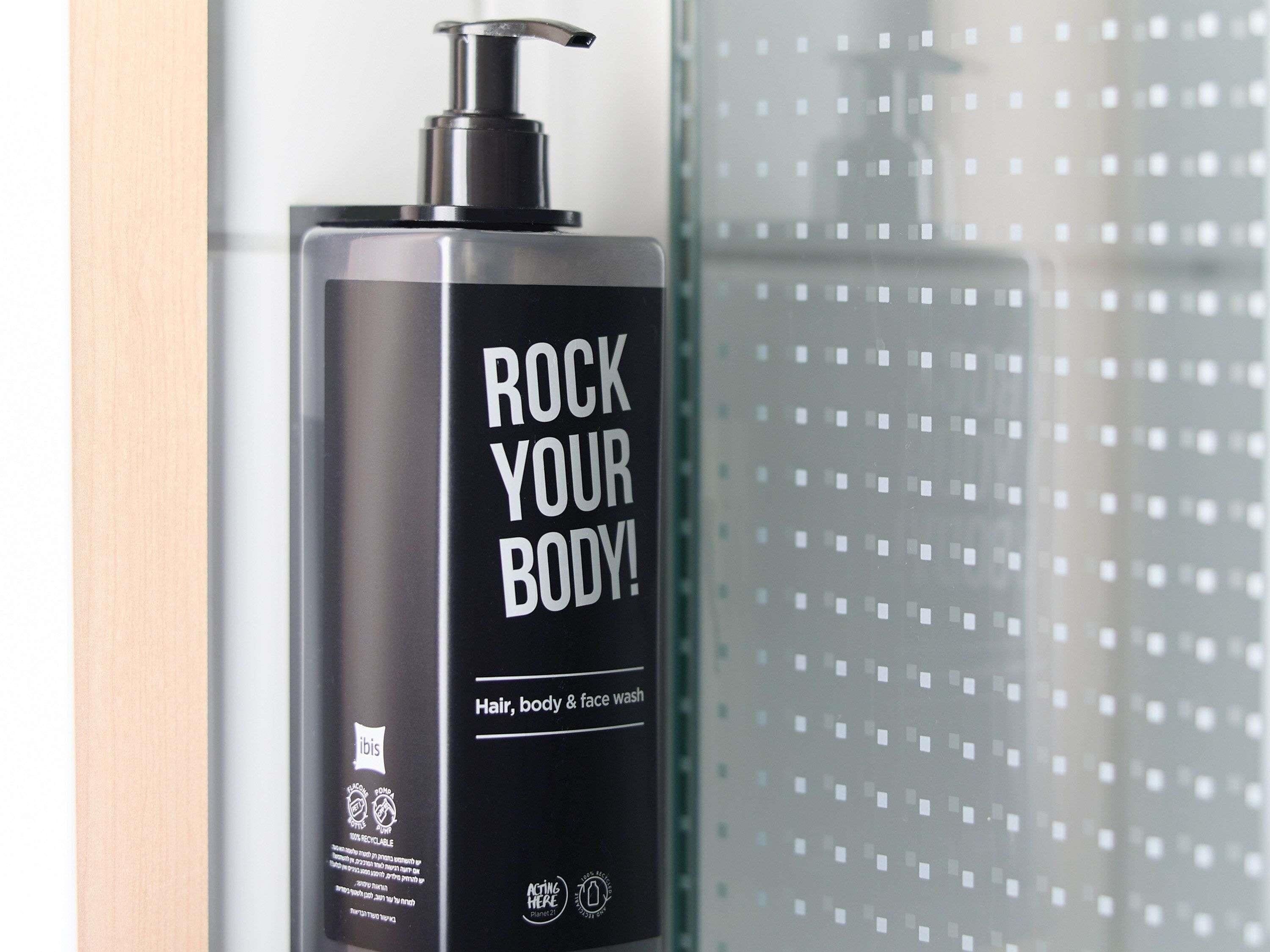 A black bottle with a pump dispenser labeled 'ROCK YOUR BODY!' and 'Hair, body & face wash' on a bathroom counter.