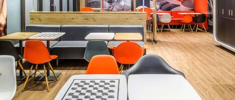 A modern cafe interior with wooden tables, orange chairs, and a central seating area.