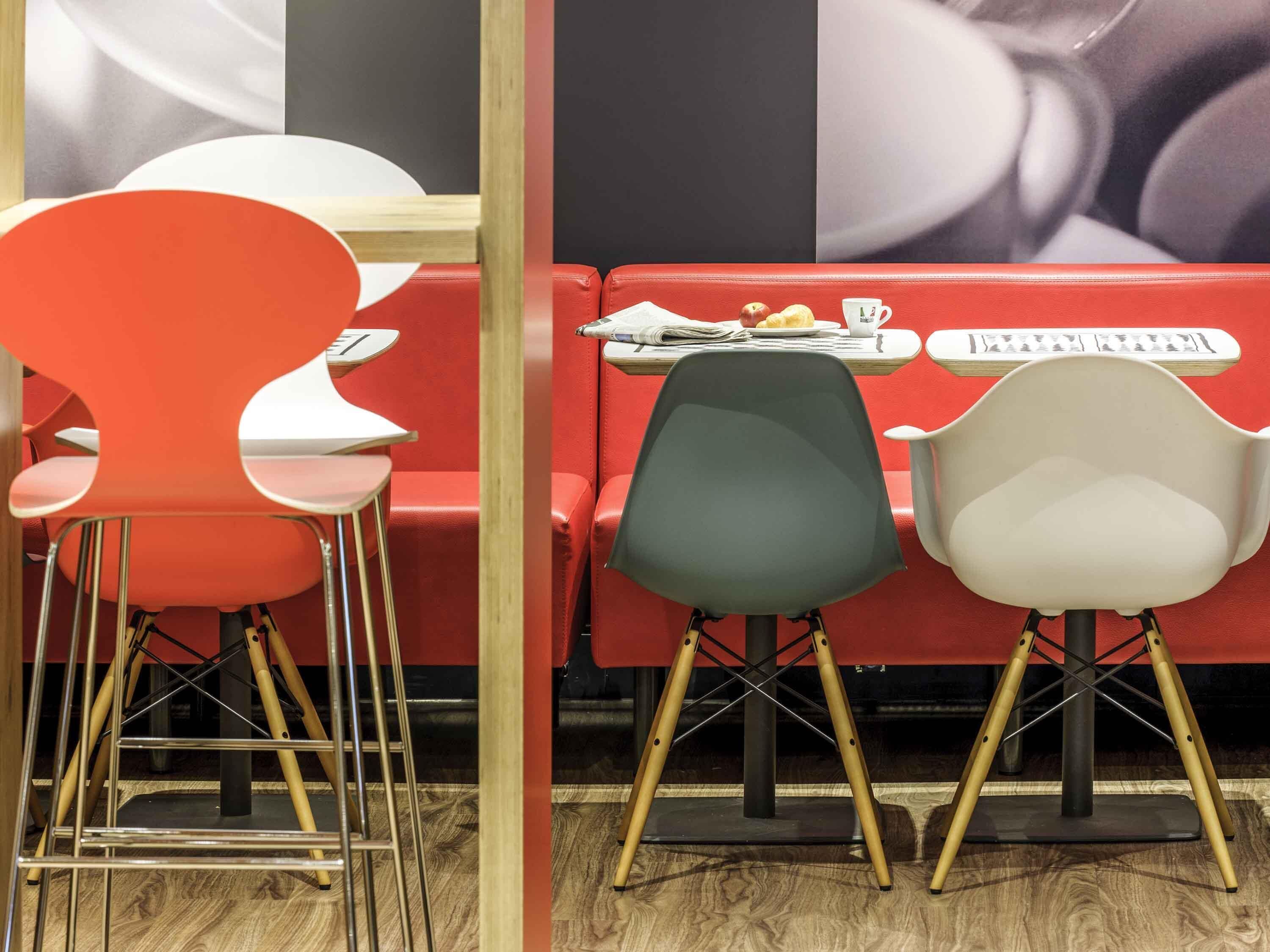 A restaurant interior with red and white chairs, a table with a newspaper, and a wall with a large poster.