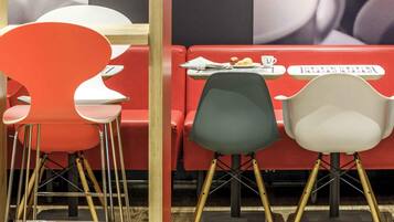 A restaurant interior with red and white chairs, a table with a newspaper, and a wall with a large poster.